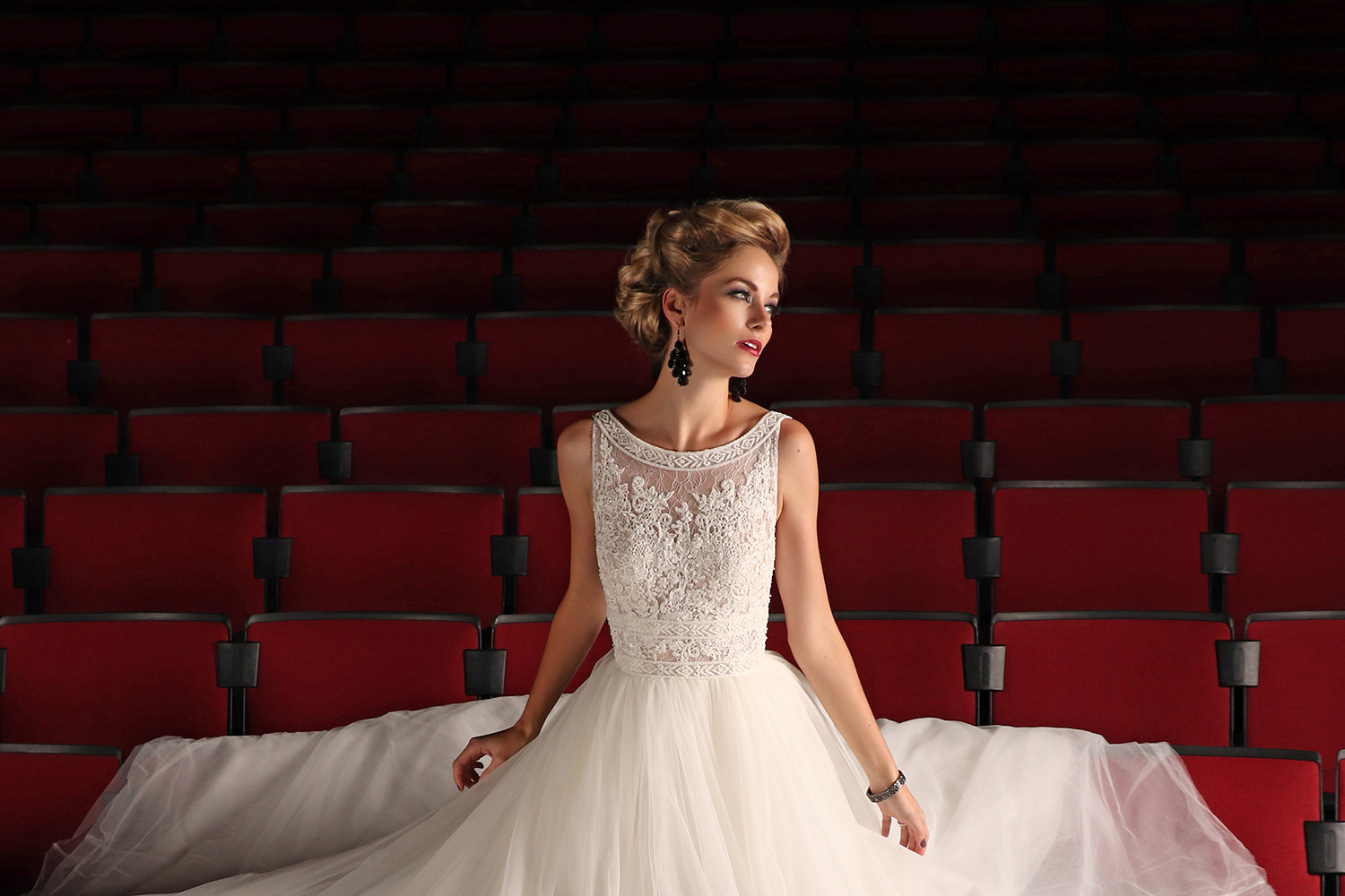 Beautiful woman in a white lace and tulle wedding dress against red theatre seats